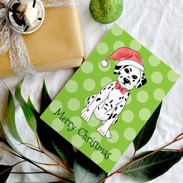 Cartoon Dalmatian in Santa Hat on a green polka dot background Christmas card next to a gift sitting on top of eucalyptus leaves.