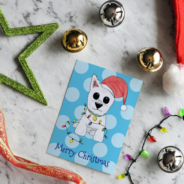 Blue polka dot Christmas card featuring Westie, Alf, in a Santa hat and wrapped in Christmas lights on a marble background surrounded by Christmas decorations.