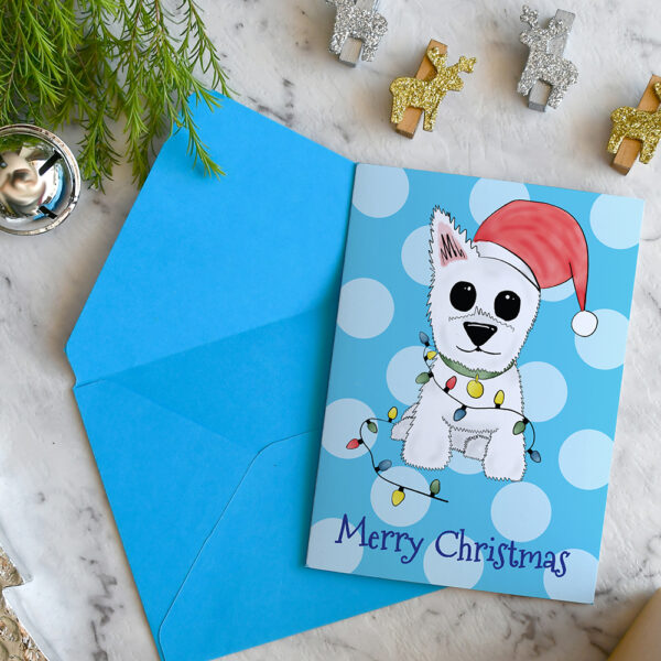 Blue polka dot Christmas card featuring Westie, Alf, in a Santa hat and wrapped in Christmas lights on a marble background surrounded by Christmas decorations and greenery.