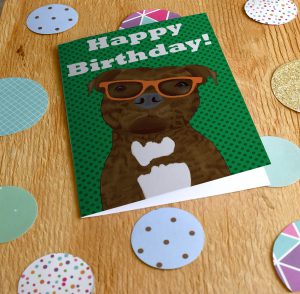 Brindle Staffy Buddy on a birthday card wearing orange glasses on a green background