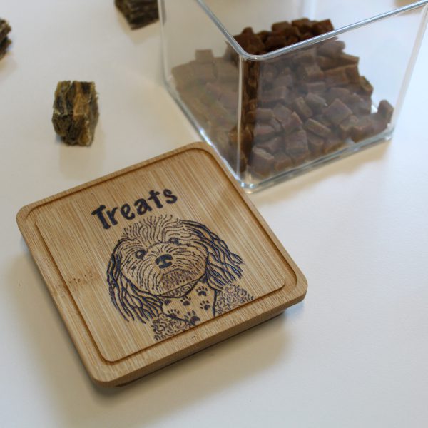 A plastic treat box with a wooden lid with the image of a cavoodle in a bandana burned into it.